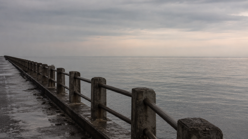 黄昏海堤，栏杆斜穿画面直到远端，尽头是空的海天交界，没有任何主体