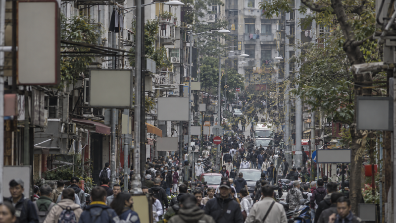 一条街上前后排开的许多层:招牌、行人、树、楼,在长焦的等同框画面里尺寸互相靠拢、彼此重叠,堆成一层密实的墙